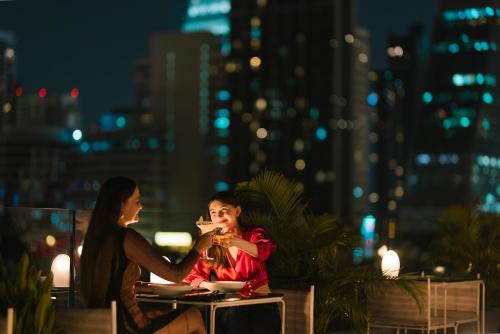 a man and a woman sitting at a table at night at Public House Bangkok, a Member of Design Hotels in Bangkok