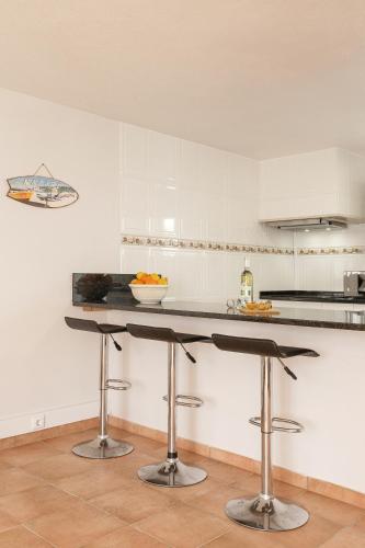 a kitchen with white cabinets and a counter with stools at Moradia Marques in Nazaré