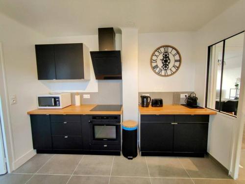 une cuisine avec des armoires noires et une horloge murale dans l'établissement Mare - Séjour à Auxerre, à Auxerre