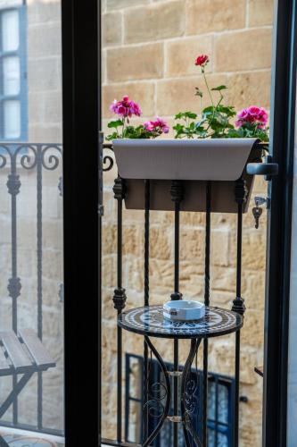 a planter on a stand with flowers on a balcony at Bell & Beam - A Timeless Gozitan Stay in Victoria in Victoria