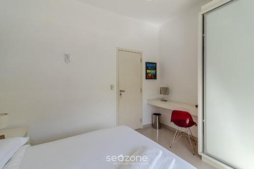 a bedroom with a white bed and a red chair at Apto térreo a 5min da Praia do Forte EMA101 in Škorak