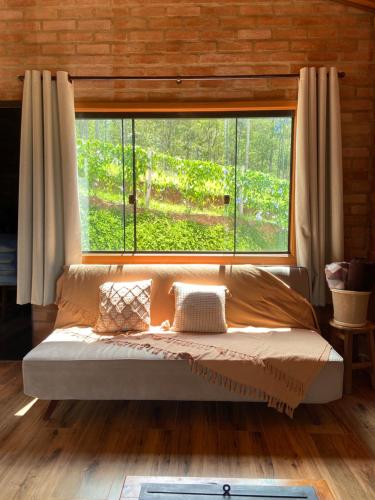 a bed in a room with a large window at Chalé Magia do Serrano in São Bento do Sapucaí