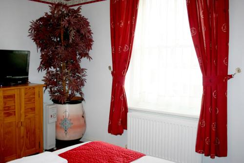 a bedroom with red curtains and a window at Ilfracombe House Hotel - near Cliffs Pavilion in Southend-on-Sea