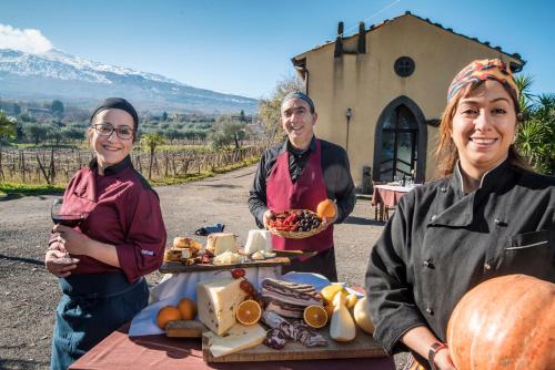 two women and a man standing next to a table of food at Agriturismo Borgo San Nicolao in Randazzo