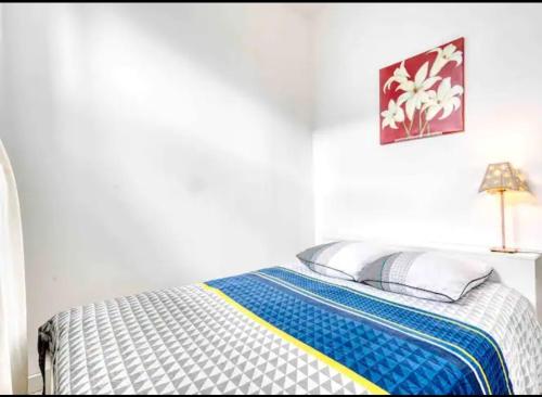 - une chambre blanche dotée d'un lit avec une couverture bleue et jaune dans l'établissement Basilique IX, à Douvres-la-Délivrande