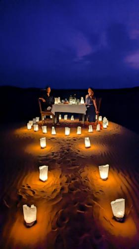 a couple of people sitting at a table in the sand at Khadija Desert Camp in Merzouga