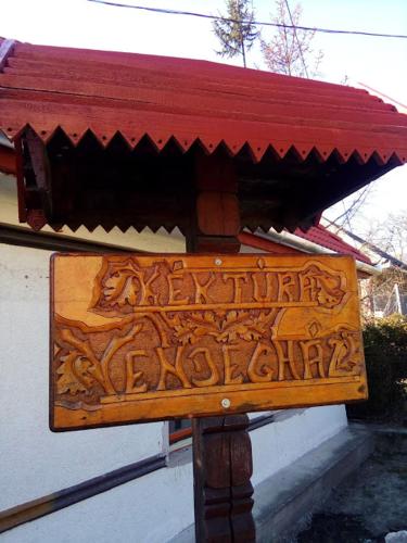 a sign in front of a building with a red roof at Kék-Túra Vendégház in Füzér