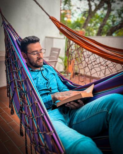 a man sitting in a hammock reading a book at Laureles Guest House LGH Hotel in Medellín
