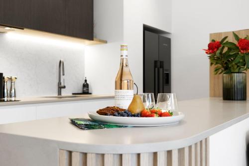 a bottle of wine and a plate of fruit on a kitchen counter at Mod House Ocean Grove- Walk to the shops, cafes, beach and park! Brand new luxury apartment in gated complex in Ocean Grove