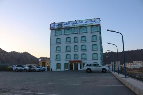 a large white building with cars parked in a parking lot at Al Karam Hotel Apartment in Nizwa