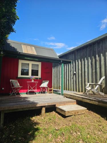 a red house with two chairs and a table on a deck at Forest Waters Raspberry Dream Cabin in Haruru
