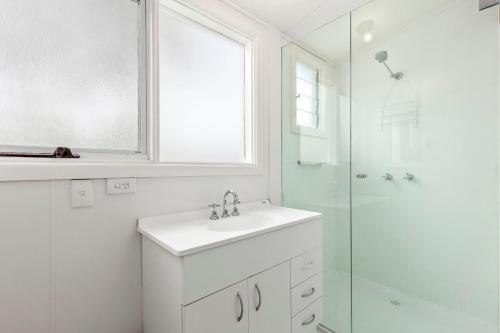 een witte badkamer met een wastafel en een douche bij Springs Beach House in Point Lonsdale