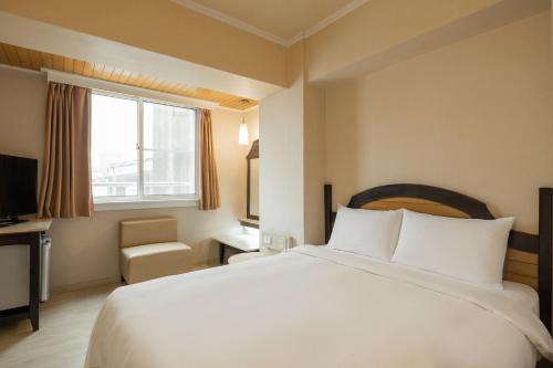 a bedroom with a large white bed and a window at Kindness Hotel - Weiwuying Branch in Kaohsiung