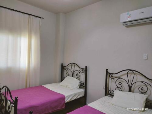 a bedroom with two beds with purple sheets and a window at شاليه مصيفي فاخر قرية لاسيرينا الساحل الشمالي in Dawwār Ḩājj as Sayyid Rizq