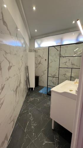La salle de bains est pourvue d'un lavabo blanc et de murs en marbre. dans l'établissement LE REX Nice, à Nice