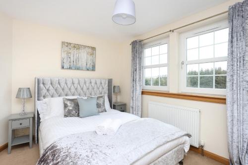 a bedroom with a bed and two windows at JOIVY Greenknowes Farmhouse with Hot Tub and Bar in Kelty