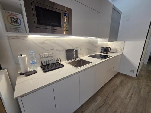 a white kitchen with a sink and a microwave at El Patio de Vespasiano- San Juan- vistas al ayuntamiento junto al puerto in Castro-Urdiales
