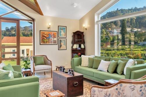 a living room with green couches and a large window at SaffronStays Coonoor Canvas in Coonoor