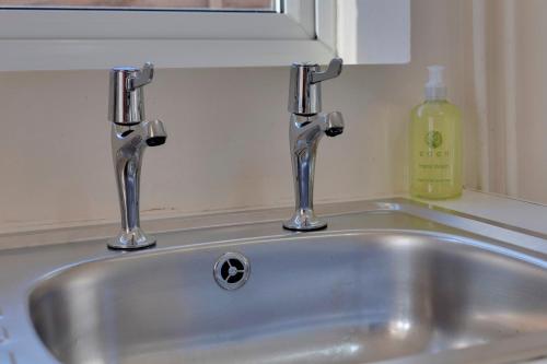 a sink with two faucets and a bottle of soap at Charming Semi-attached bungalow with free parking Pass the Keys in Cambridge