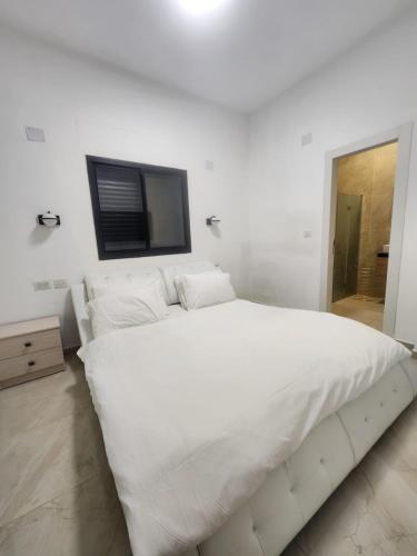 a white bedroom with a large white bed and a television at הצימר של הילה in Qasrîne