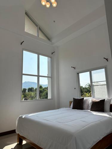 a white bedroom with a large bed with windows at บ้านสวนสุรัชฎา ปาย in Kampong Huaibū