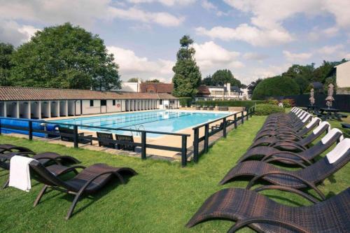 a swimming pool with chaise lounges and chairs in the grass at Dancenter Boutique Luxury Gatwick Airport in Dorking