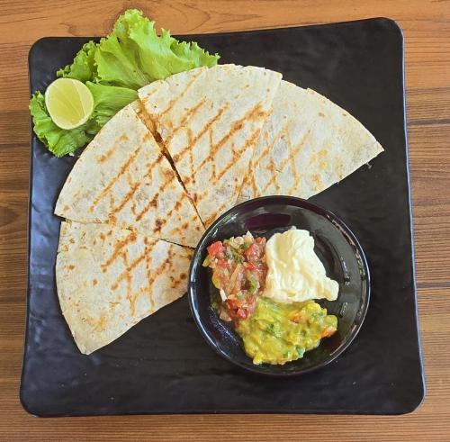 a black plate with a tortilla and a bowl of guacamole at Makarma Resort Lombok in Senggigi 