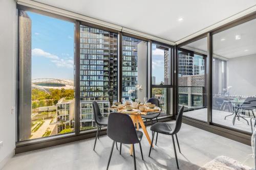 a dining room with a table and chairs and large windows at New 2BR Apartment in Olympic Park Near Stadium in Sydney