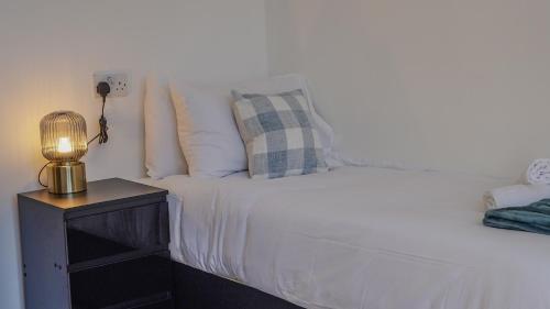 a bed with white sheets and a lamp on a night stand at Spacious Bromley Home w Free parking and Outside Dining in Bromley