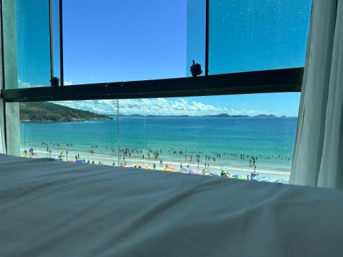 a view of a beach from a bedroom window at Arraial do cabo loft prainha in Arraial do Cabo