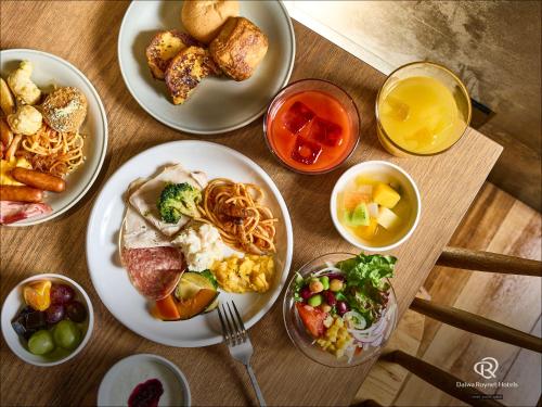 a wooden table topped with plates of food and drinks at DEL style Osaka-Shinsaibashi by Daiwa Roynet Hotel in Osaka