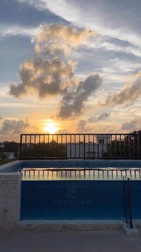 a large swimming pool with a sunset in the background at Hotel Zendero Tulum in Tulum