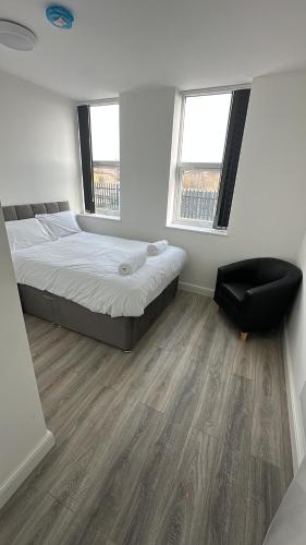 a bedroom with a bed and a chair and two windows at 2 Bed Sizeable Station House Apartment - Free Wifi, Parking & EV in Scunthorpe