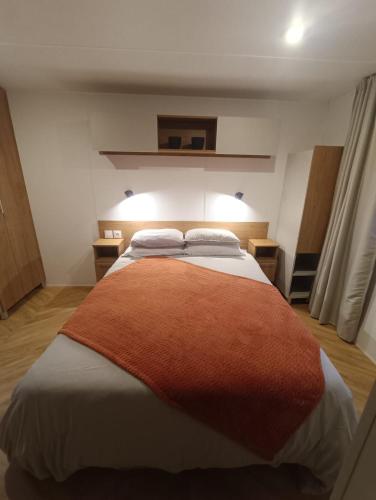 une chambre avec un grand lit avec une couverture orange dans l'établissement Mobile home Grand confort, à Lège-Cap-Ferret
