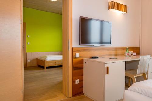 a room with a tv and a desk with a table at Allegria Resort Stegersbach - Allegria Hotel in Stegersbach