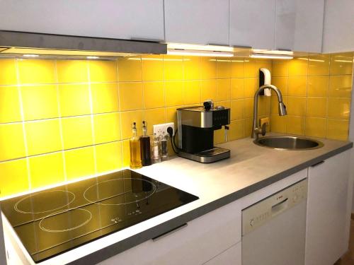 - une cuisine avec un évier et du carrelage jaune sur le mur dans l'établissement En cœur de ville et climatisé - Le Off Sète, à Sète