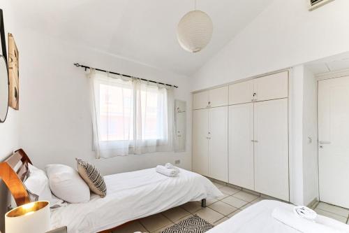 a white bedroom with a bed and a window at Limnaria Gardens Beautiful Apartment by VICHY in Paphos