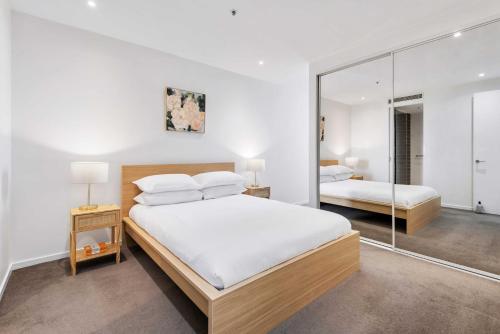 a white bedroom with two beds and a mirror at Stylish 2-Bed Apartment Near MCG in Melbourne