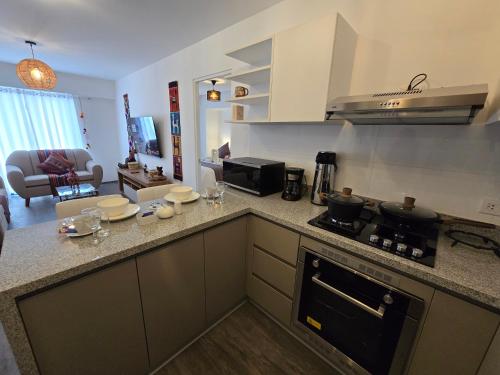 a kitchen with a stove top oven next to a living room at Acogedor Departamento en Cusco, Ideal para Familias y Amigos, Equipado y Céntrico in Cusco