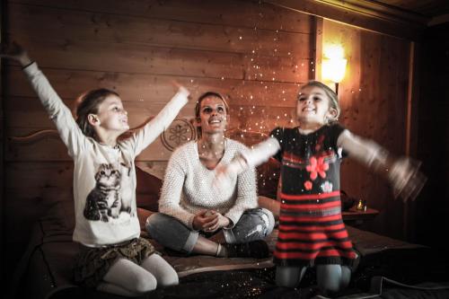 two girls and a woman sitting on a bed with their arms up at Hôtel Le Refuge in Tignes