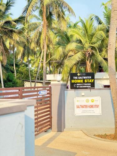 a home stay sign in front of a fence with palm trees at Sw by The Saltwater Homestay in Udupi