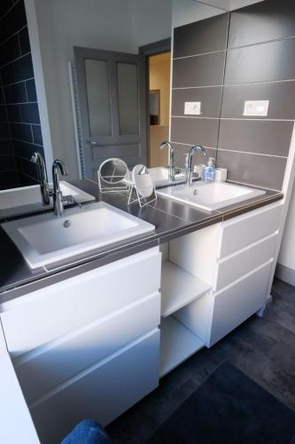 La salle de bains est pourvue de 2 lavabos et de placards blancs. dans l'établissement La Maison d'à coté, à Naucelle
