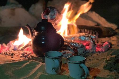 a pot and two cups in front of a fire at Oasis Panorama in Bawiti