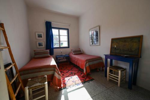 a room with two beds and a desk and a window at Hotel-Restaurant Le Kaouki in Sidi Kaouki