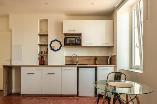une cuisine avec des armoires blanches et une table en verre dans l'établissement Studio Blue Délice, à Narbonne