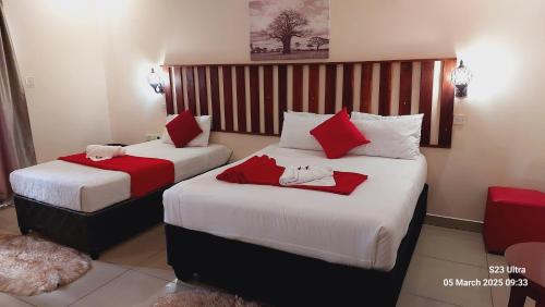 two beds in a hotel room with red and white sheets at Comfort Palace Guest House Kasane in Kasane