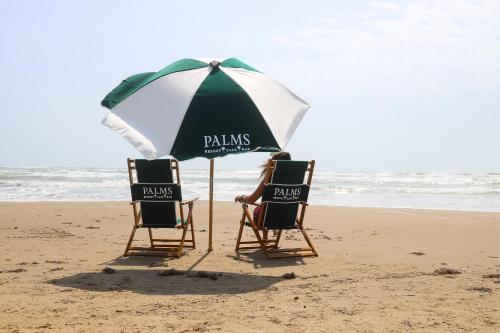 two people sitting in chairs under an umbrella on the beach at Palms Resort & Cafe on the Beach in South Padre Island