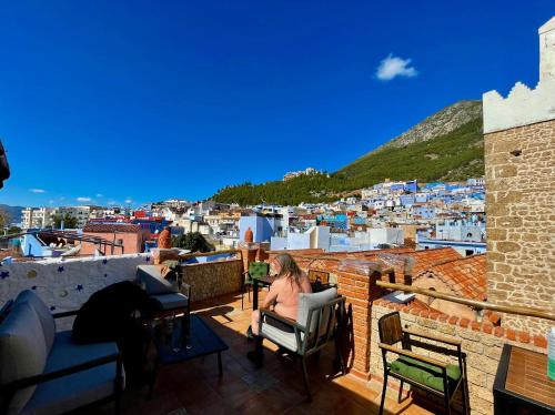 a woman sitting on a balcony overlooking a city at Hotel Abi khancha in Chefchaouene