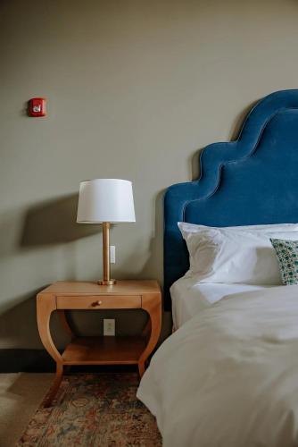 a bed with a blue headboard and a table with a lamp at The Woodward Hotel in Macon