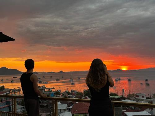 a man and a woman standing on a balcony watching the sunset at De Nata in Labuan Bajo